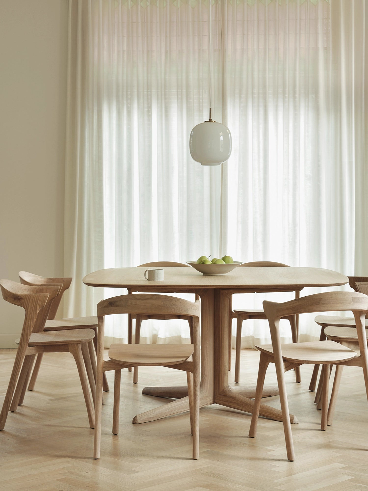 Ethnicraft Corto Dining Table in natural light oak, square shape, styled in a bright, minimalist dining area with matching wooden chairs, a candle, and blue glassware, creating a serene ambiance.