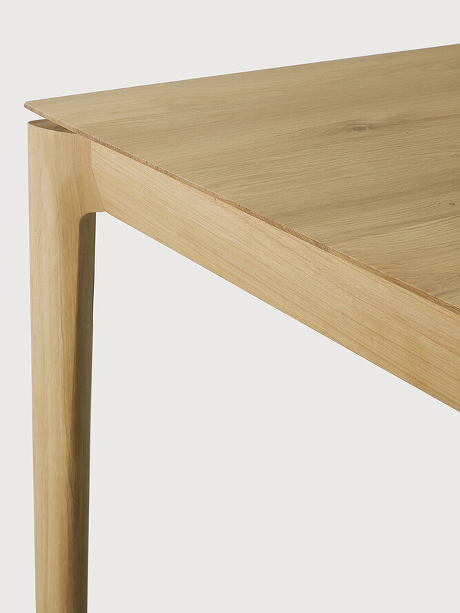 Ethnicraft Bok Dining Table, a detailed shot of the solid oak tabletop and leg, showcasing the smooth, rounded edges and the rich, natural wood grain. The elegant and sturdy construction is clearly visible.