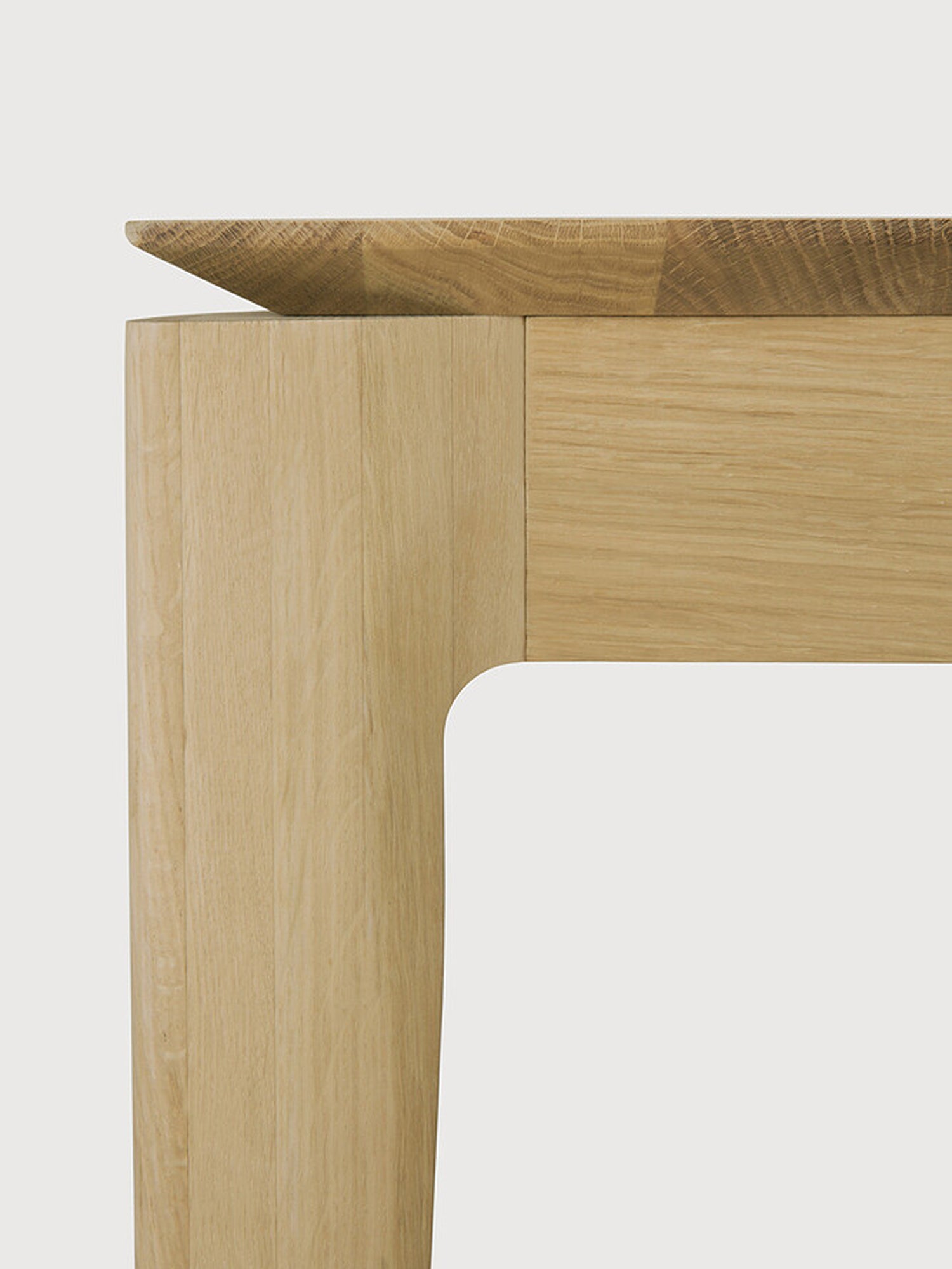 Ethnicraft Bok Dining Table, a close-up detail of the corner where the solid oak tabletop meets the leg. The exquisite craftsmanship, visible wood grain, and seamless joinery of the premium oak are highlighted.
