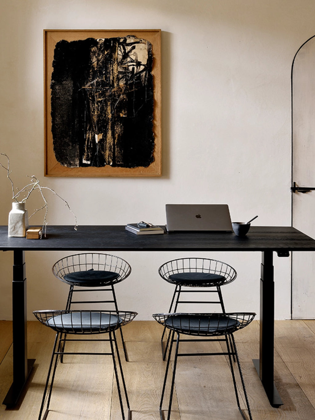 Ethnicraft Bok Adjustable Desk in a sophisticated black finish, with a dark tabletop and black adjustable frame, accompanied by two elegant black wire chairs in a contemporary setting.