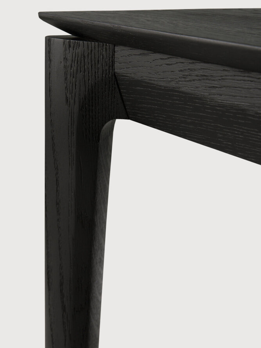 Ethnicraft Bok Bench, a modern minimalist solid black oak bench featuring a sleek, durable design with visible wood grain texture. It highlights clean lines and an elegantly curved leg joint, showcasing expert craftsmanship in dark, charcoal-toned wood. Perfect as a Scandinavian dining bench or a contemporary entryway bench for design-conscious homes.