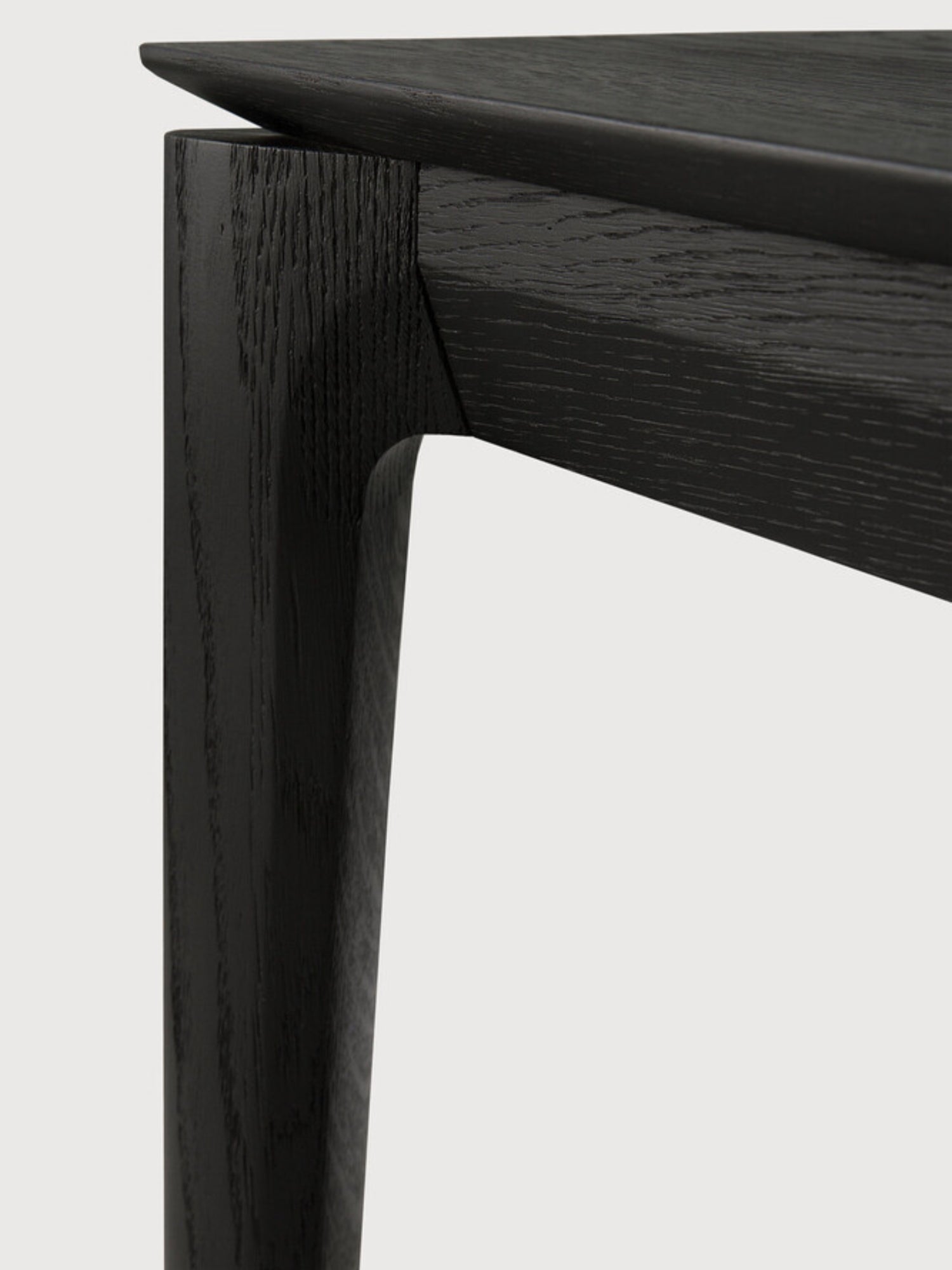 Ethnicraft Bok Bench, a modern minimalist solid black oak bench featuring a sleek, durable design with visible wood grain texture. It highlights clean lines and an elegantly curved leg joint, showcasing expert craftsmanship in dark, charcoal-toned wood. Perfect as a Scandinavian dining bench or a contemporary entryway bench for design-conscious homes.