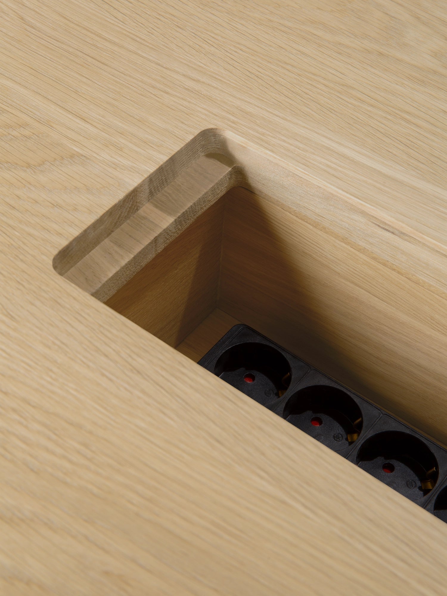 Ethnicraft Geometric Meeting Table, a modern minimalist dining or meeting table crafted from light natural solid oak wood, featuring a seamlessly integrated black power strip with multiple outlets for convenient charging and connectivity. This contemporary oak table is ideal for a Scandinavian-inspired dining room, a productive home office, or a stylish conference space.