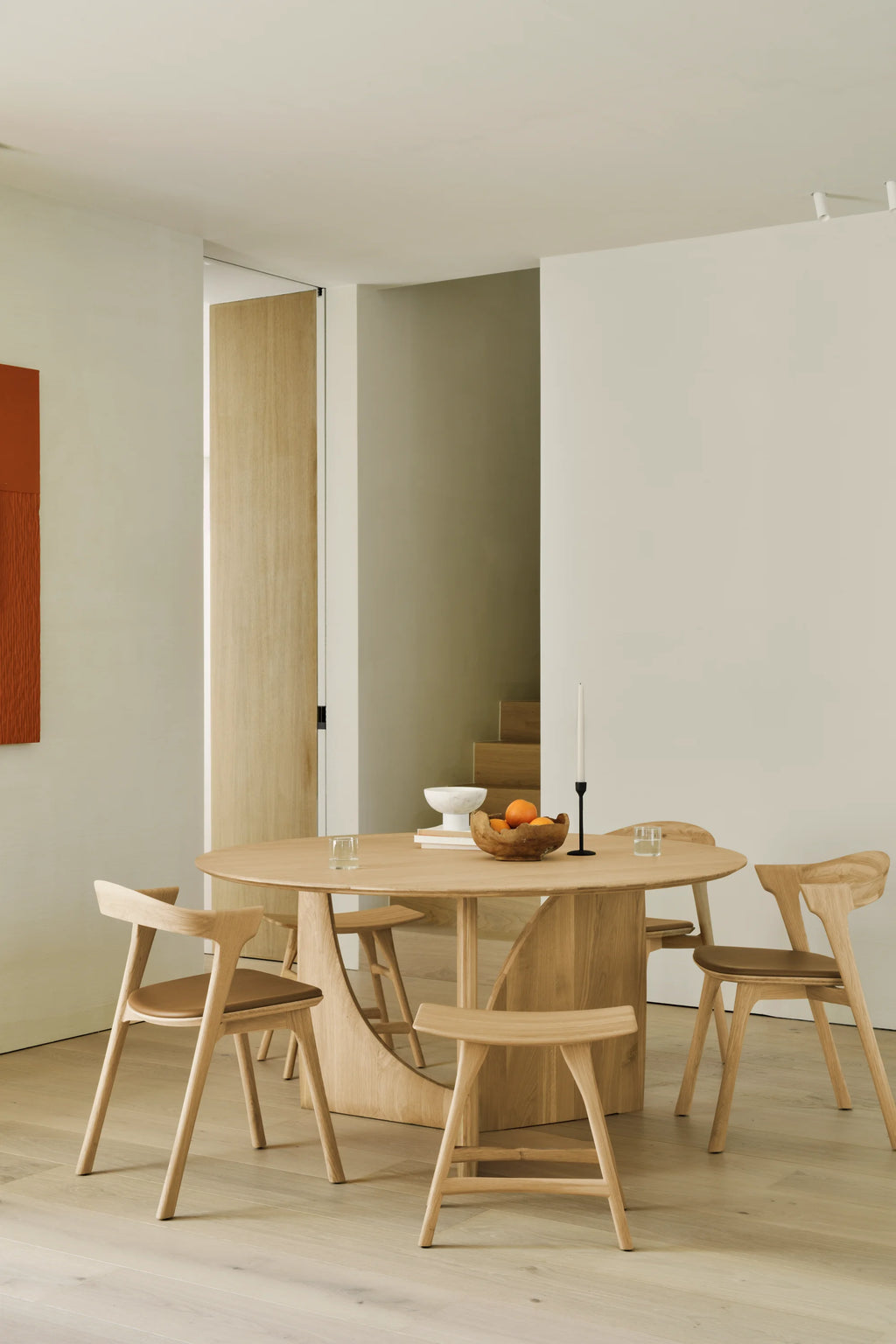 Ethnicraft Geometric Round Dining Table, a modern minimalist dining table crafted from light natural solid oak wood with a smooth round tabletop and a distinctive, sculptural geometric base. This contemporary oak dining table offers clean lines and an organic modern aesthetic, perfect for a Scandinavian dining room or open-plan living space.