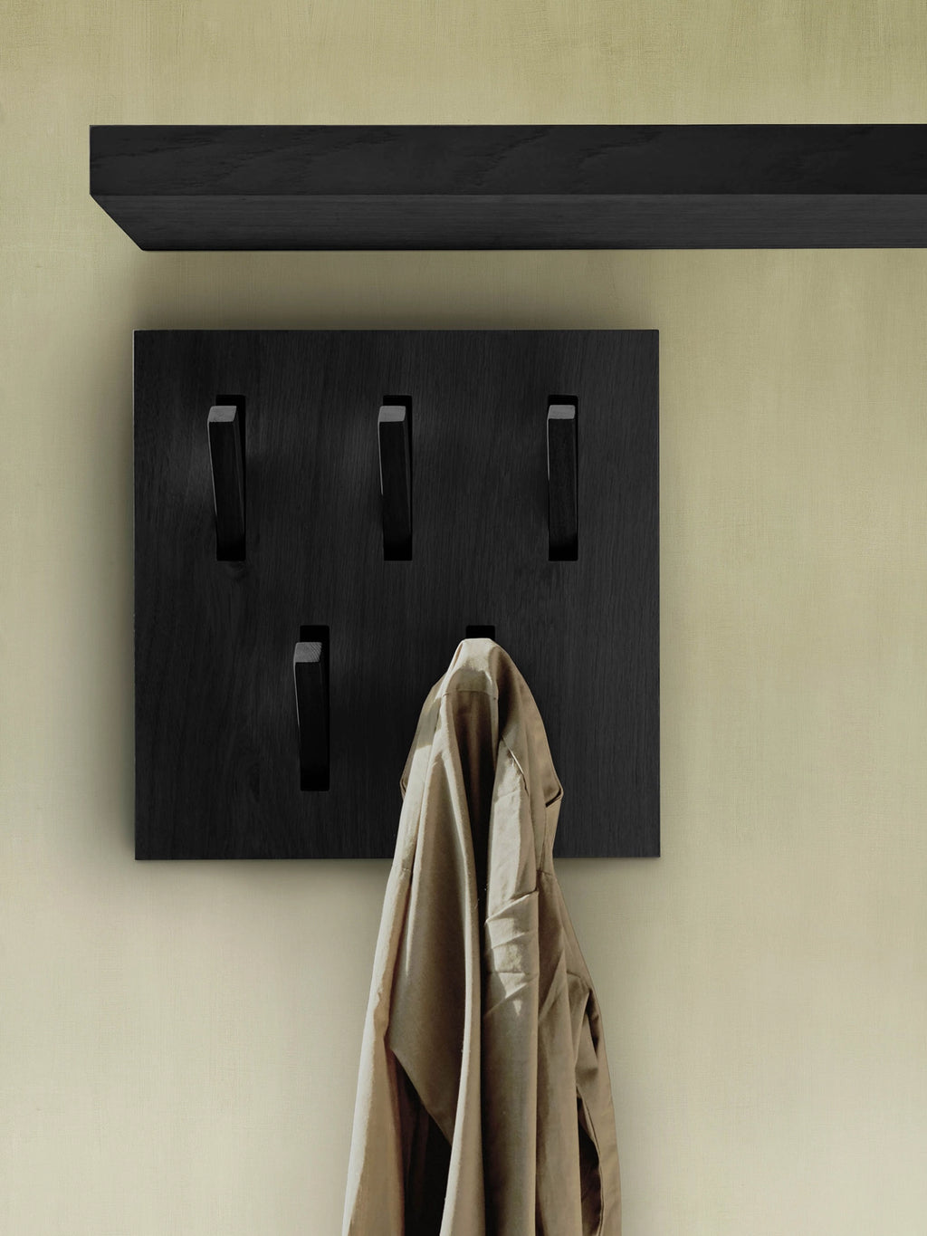 Ethnicraft Utilitile Wall Hanger, a sleek modern minimalist coat rack crafted from solid black oak wood with five innovative, flush-mounted hooks that seamlessly recess when not in use, offering a clean, contemporary aesthetic. This functional wall-mounted organizer also features a matching floating shelf above for additional storage or display. Ideal for a Scandinavian entryway, modern hallway organization, or a minimalist bedroom.