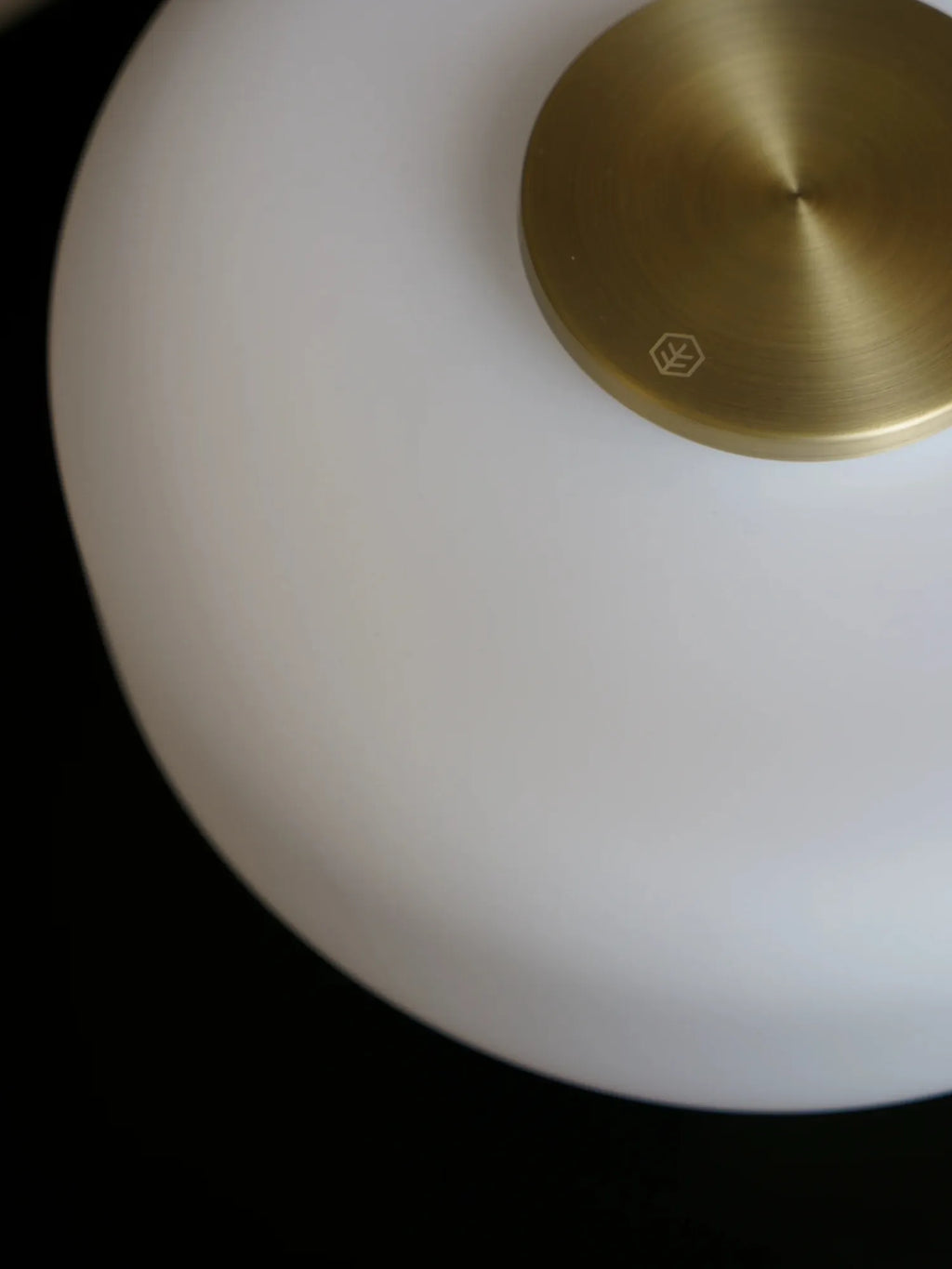 TAMO Fonte Table Lamp, an elegant close-up of a white matte glass diffuser with a premium brushed brass top featuring a subtle etched logo. Perfect for ambient lighting.