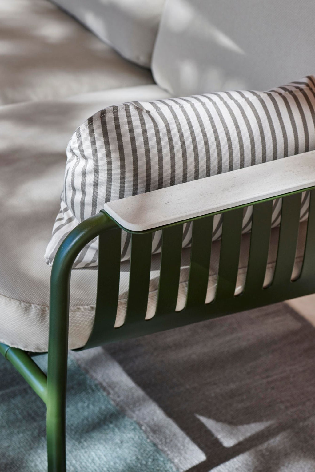 Gandia Blasco Capa 2-Seat Sofa, a modern outdoor sofa featuring a matte dark green aluminum frame with a distinctive slatted design, plush light grey outdoor fabric cushions, and sleek white composite armrests. It is accented with a stylish grey and white striped lumbar pillow, ideal for contemporary patio furniture or minimalist garden lounge areas.