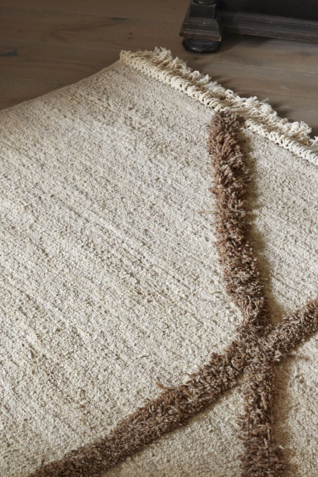 Sera Helsinki Vuoristo Rug, a luxurious hand-knotted wool area rug featuring a plush cream-colored body with a distinctive brown shaggy abstract pattern and natural fringed edges. This high-pile textured rug offers cozy warmth and organic modern style. Ideal for bohemian living rooms, Scandinavian bedrooms, or rustic home decor.