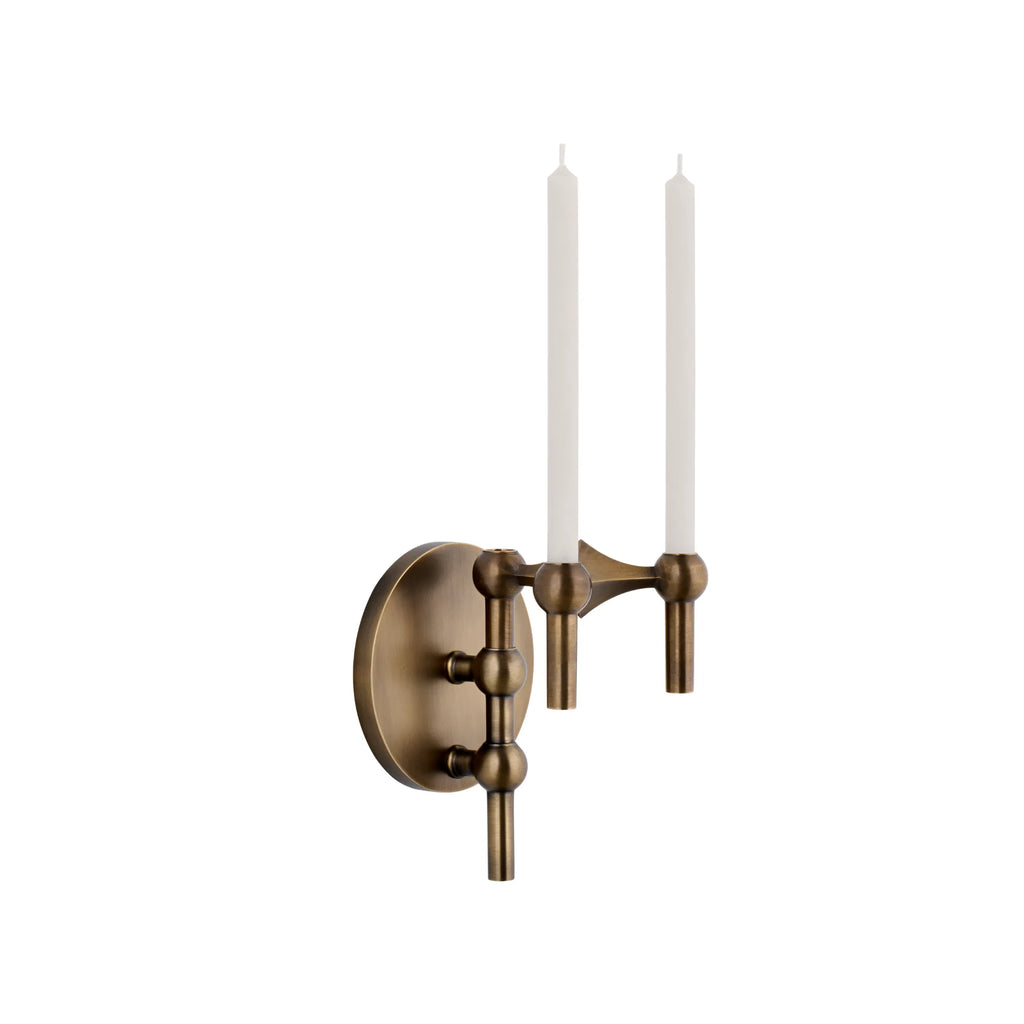 Stoff Nagel Wall Hanger Candle Holder - Bronzed Brass - Configuration 1, a modular mid-century modern wall-mounted candle holder crafted from brushed bronzed brass with a rich antique finish, featuring a round base plate and two cylindrical arms with spherical joints holding slender white taper candles. This sculptural metal wall decor piece is perfect for creating ambient lighting in minimalist living rooms, industrial chic dining areas, or contemporary entryways.