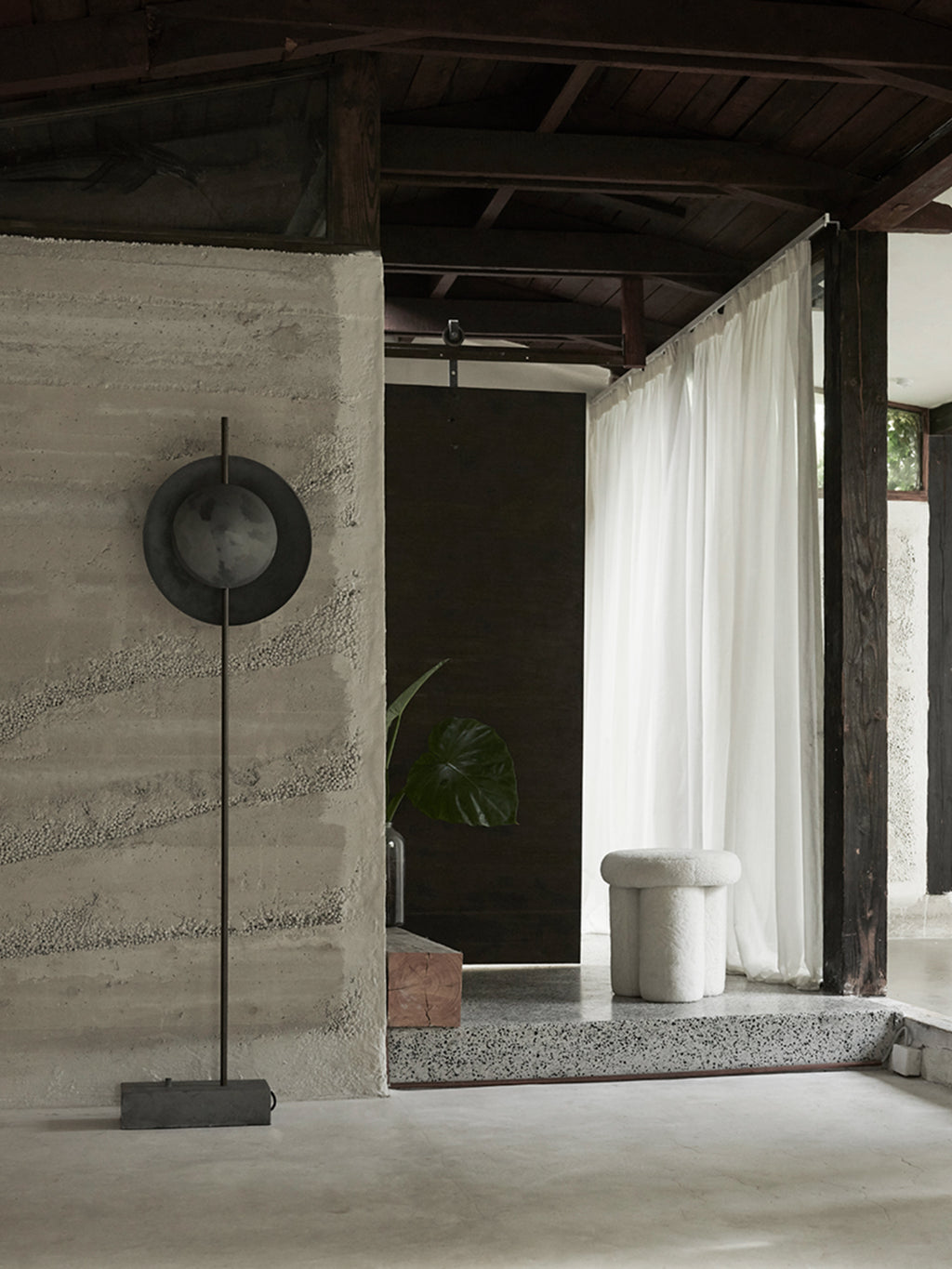 101 CPH Dawn Floor Lamp, a premium matte black metal lamp with layered circular shades, standing on a textured concrete-like base in a modern brutalist interior. Provides ambient lighting.
