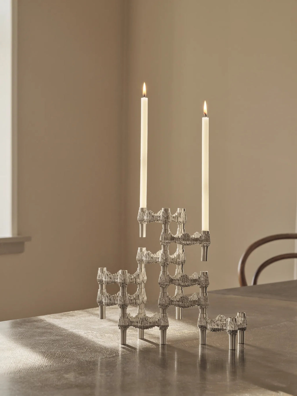 Stoff Nagel Quist Candle Holder, a modular chrome-plated metal candle holder with a distinctive brutalist texture and a shiny silver finish, designed for stackable and customizable arrangements. Its iconic sculptural form allows for endless configurations, creating a dynamic centerpiece. Perfect for contemporary dining tables, industrial chic living rooms, or modern minimalist decor.