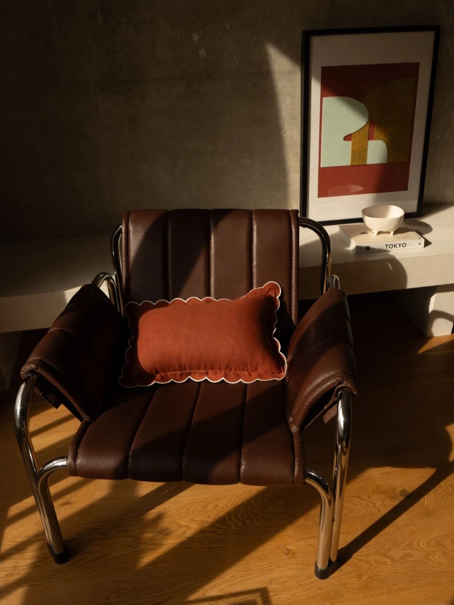 Brown leather chair with a pillow in a room with a framed picture on the wall.