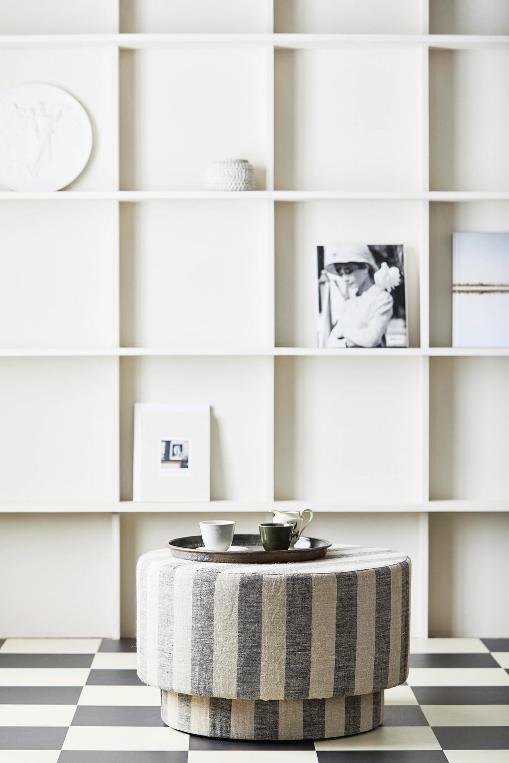 Striped ottoman in a room with white shelving and checkered floor.