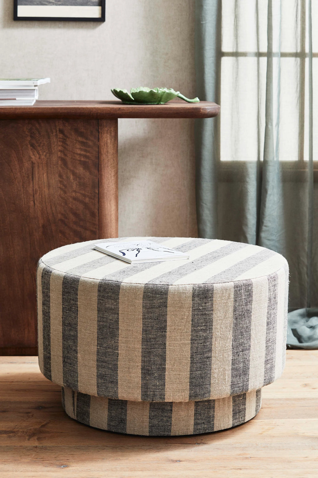 Striped ottoman in a room with wooden furniture and a window.
