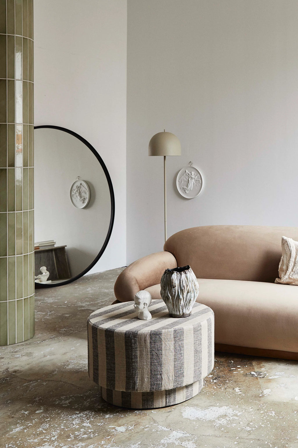 Modern living room with a beige sofa, round ottoman, and decorative elements.