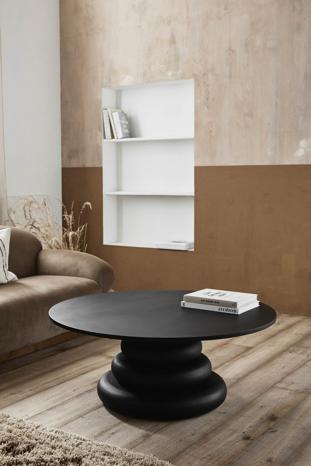 Nordal Yalu Coffee Table, a striking contemporary round coffee table featuring a smooth matte black finish and a unique sculptural stacked-ring base. This organic modern design offers a bold statement piece crafted from durable materials, perfect for a minimalist living room or brutalist-inspired interior.
