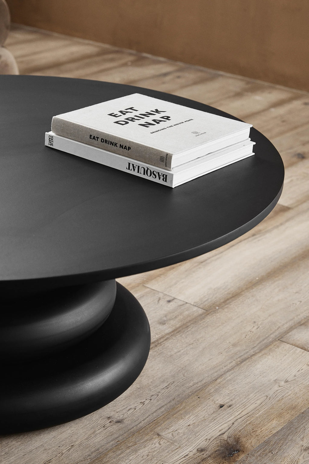 Nordal Yalu Coffee Table, a modern minimalist round coffee table crafted from matte black finished wood, featuring a smooth, flat circular tabletop. Its distinctive sculptural pedestal base showcases a stacked, rounded silhouette, adding an organic modern touch. This contemporary black coffee table is perfect for elegant living rooms and minimalist or organic modern interiors.