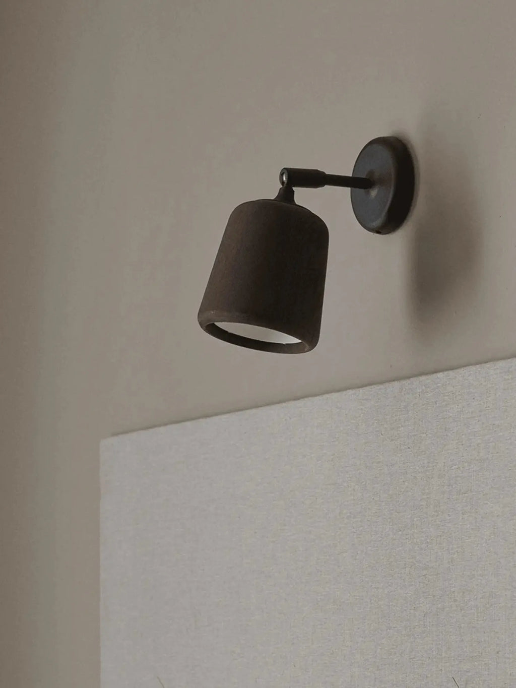 New Works Material Wall Lamp: close-up of a premium dark gray sconce with a conical, textured shade and black metal arm, against a beige wall. Ideal for contemporary interior lighting.