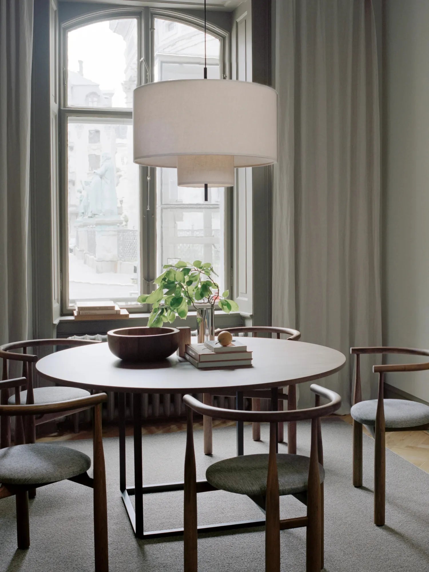 New Works Margin Pendant Lamp with a stacked, off-white textile shade and black suspension, hanging above a round Scandinavian dining table. A premium lighting solution.