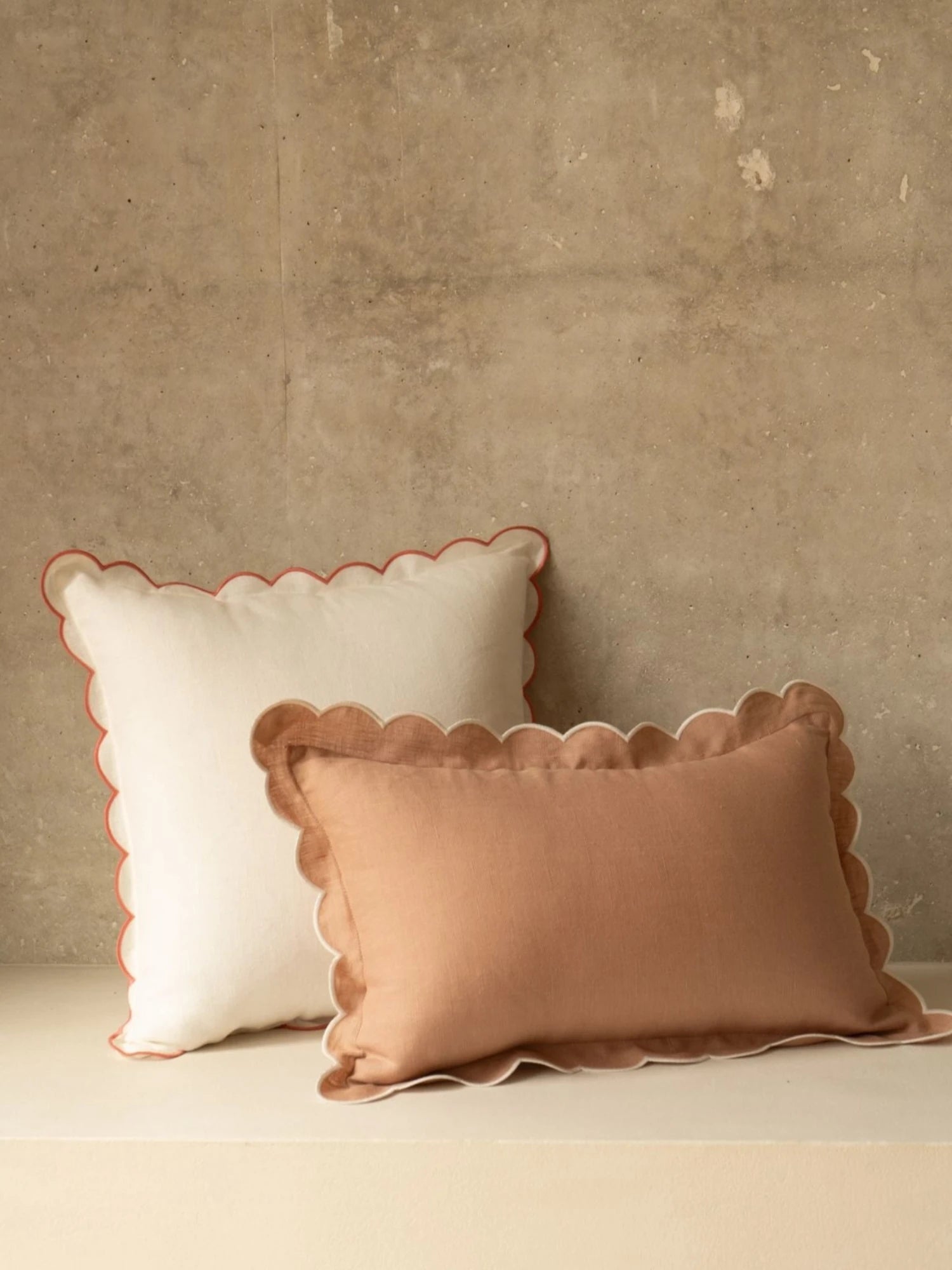 Two decorative pillows with scalloped edges on a neutral background