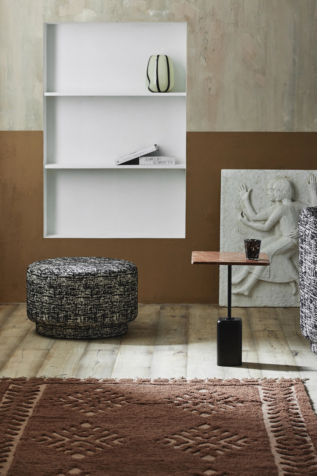 Nordal Bomu Pouf, a contemporary round ottoman upholstered in a striking black and white textured woven fabric, creating a visually rich, mottled pattern. This stylish and versatile pouf provides comfortable extra seating or a chic footrest, perfect for modern minimalist living rooms or as a unique bedroom accent.