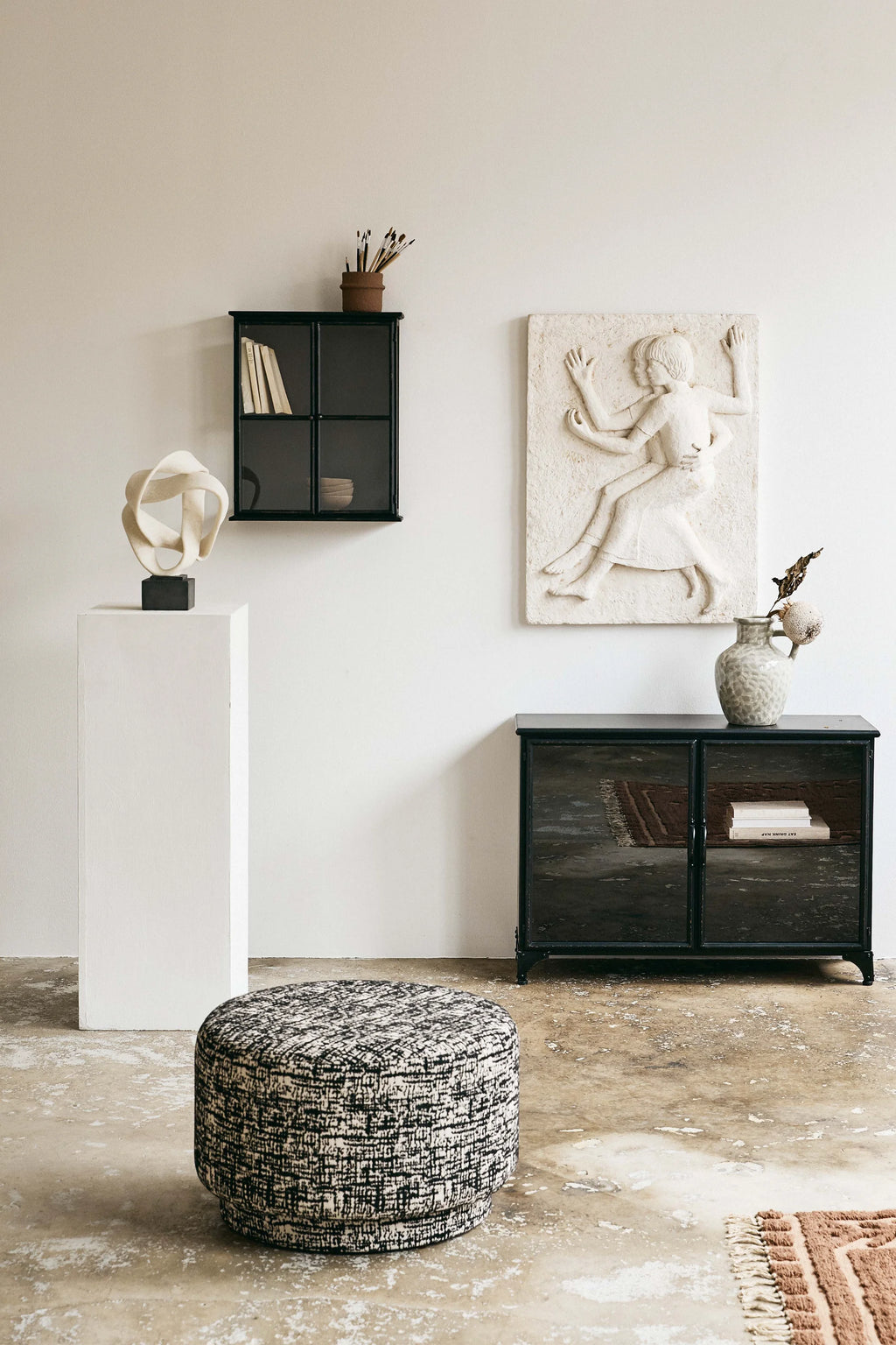 Nordal Bomu Pouf, a modern round pouf upholstered in a black and off-white textured woven fabric featuring a dynamic, abstract pattern. This contemporary ottoman offers versatile accent seating or a stylish footrest, perfect for minimalist living rooms, bedrooms, or creative studio spaces.