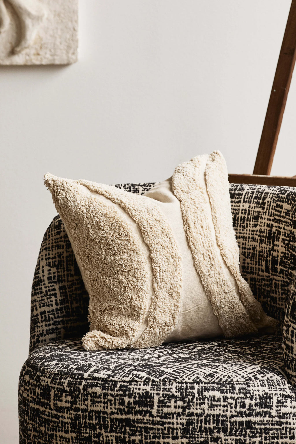 Nordal Bomu Lounge Chair, upholstered in a striking black and off-white abstract patterned fabric with a cozy, curved silhouette. It features a cream-colored decorative pillow with a shaggy, looped bouclé texture and a smooth central panel. This contemporary accent chair is perfect for adding an organic modern or boho chic touch to living rooms or bedrooms.