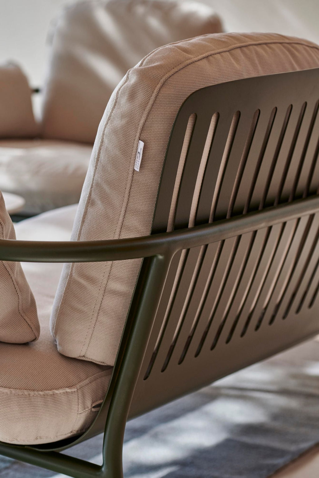 Gandia Blasco Capa 2-Seat Sofa, a contemporary outdoor sofa featuring a durable powder-coated dark green aluminum frame with a distinctive slatted backrest and gently curved armrests. It is upholstered in plush, weather-resistant light taupe outdoor fabric cushions, offering both comfort and modern minimalist style.