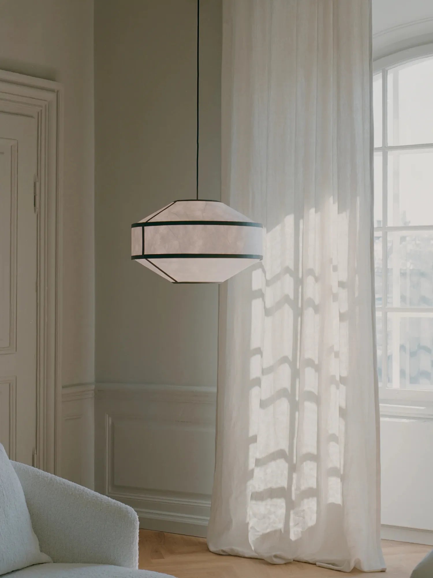 New Works Kite Pendant Lamp in a modern living space; hexagonal white paper shade with dark structural elements, hanging against a sunlit window. A premium decorative lighting piece.