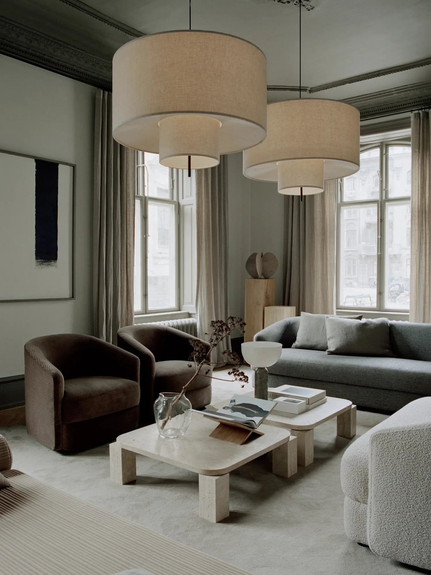 New Works Margin Pendant Lamp, featuring two tiered, natural linen drum shades, hangs in a modern living room setting. A premium, statement lighting piece.