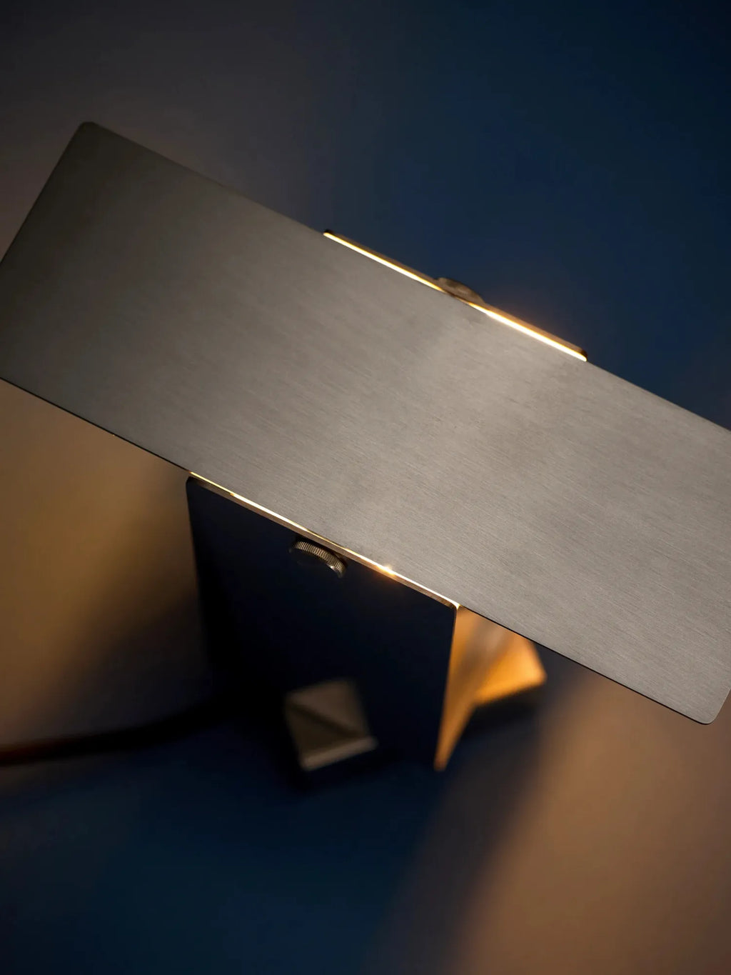 MOEBE Pivoting Table Lamp, a modern minimalist desk lamp featuring a sleek, rectangular dark grey brushed metal light panel that pivots on a matching geometric metal base, emitting a warm, focused light.