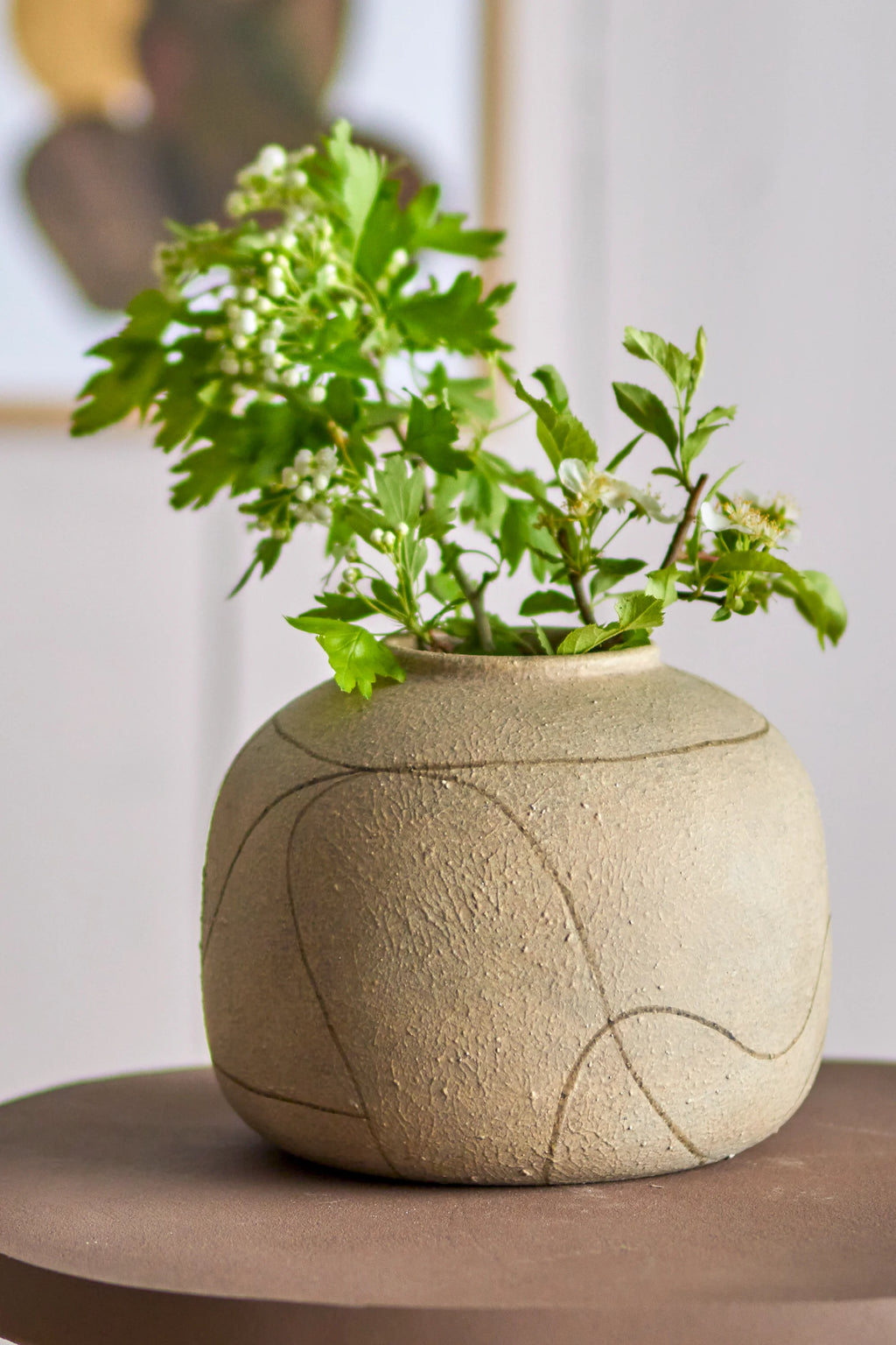 Bloomingville Niza Vase, a round, organic modern ceramic vase crafted from unglazed stoneware in a natural beige tone, featuring a heavily textured, porous finish with subtle crackling. Its globular shape is adorned with a delicate, abstract hand-drawn dark line pattern that wraps around the surface. Ideal for rustic shelf styling, minimalist living room decor, or as a contemporary natural accent in any space.