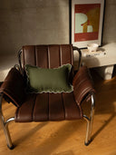Brown leather chair with a green pillow in a room with a framed picture on the wall.