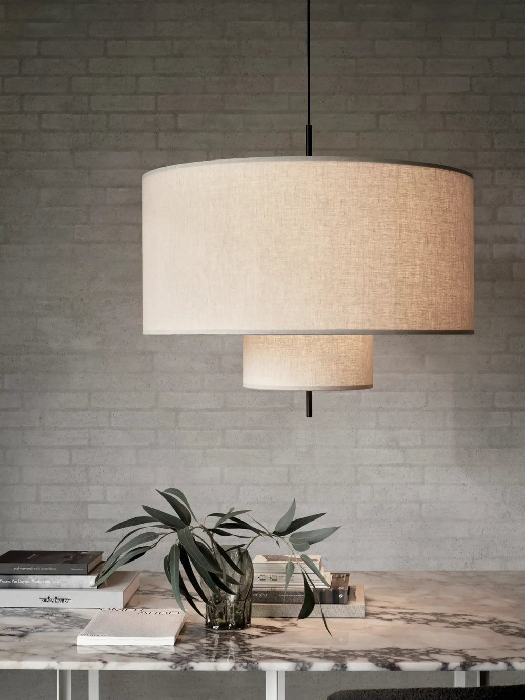 New Works Margin Pendant Lamp, a luxury tiered cream linen shade with subtle grey trim, suspended from a black cord, providing soft, ambient light in a modern setting. Ideal for sophisticated interiors.