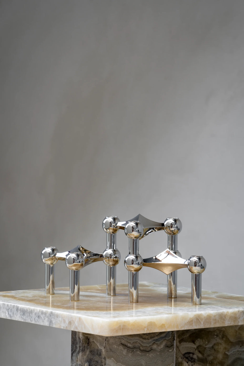Stoff Nagel Candle Holder in a polished chrome finish, showcasing its modular, sculptural design with multiple tiers of interconnected spheres and candle cups, resting on a luxurious veined marble surface.