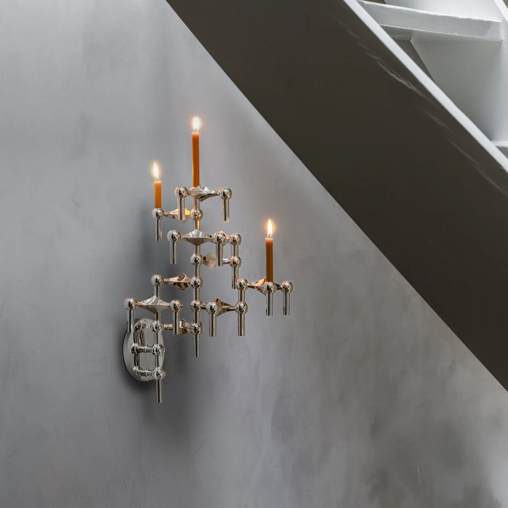 Stoff Nagel Wall Hanger Candle Holder - Chrome - Configuration 3, a striking mid-century modern and brutalist-inspired modular candle holder crafted from polished chrome metal. Its interconnected sculptural design features multiple candle cups holding amber-colored taper candles, creating an atomic-like structure mounted as a unique wall sconce. Perfect for adding a contemporary Danish design statement to living rooms, entryways, or minimalist bedrooms.