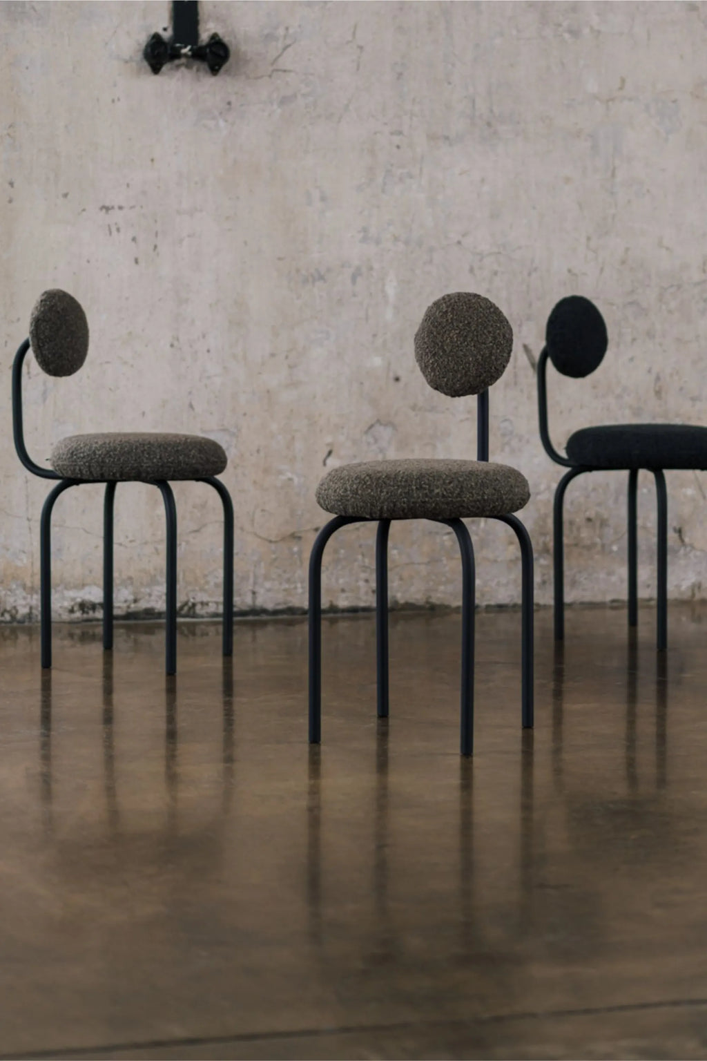 NG DESIGN Object 077 Chair, a sculptural organic modern dining chair featuring a matte black bent tubular metal frame with rounded legs and a distinct circular backrest. Upholstered in a plush, textured bouclé fabric, the chairs are available in a deep dark olive green and a classic black. This minimalist and contemporary chair is perfect for a modern dining room, chic home office, or as a sophisticated accent chair.