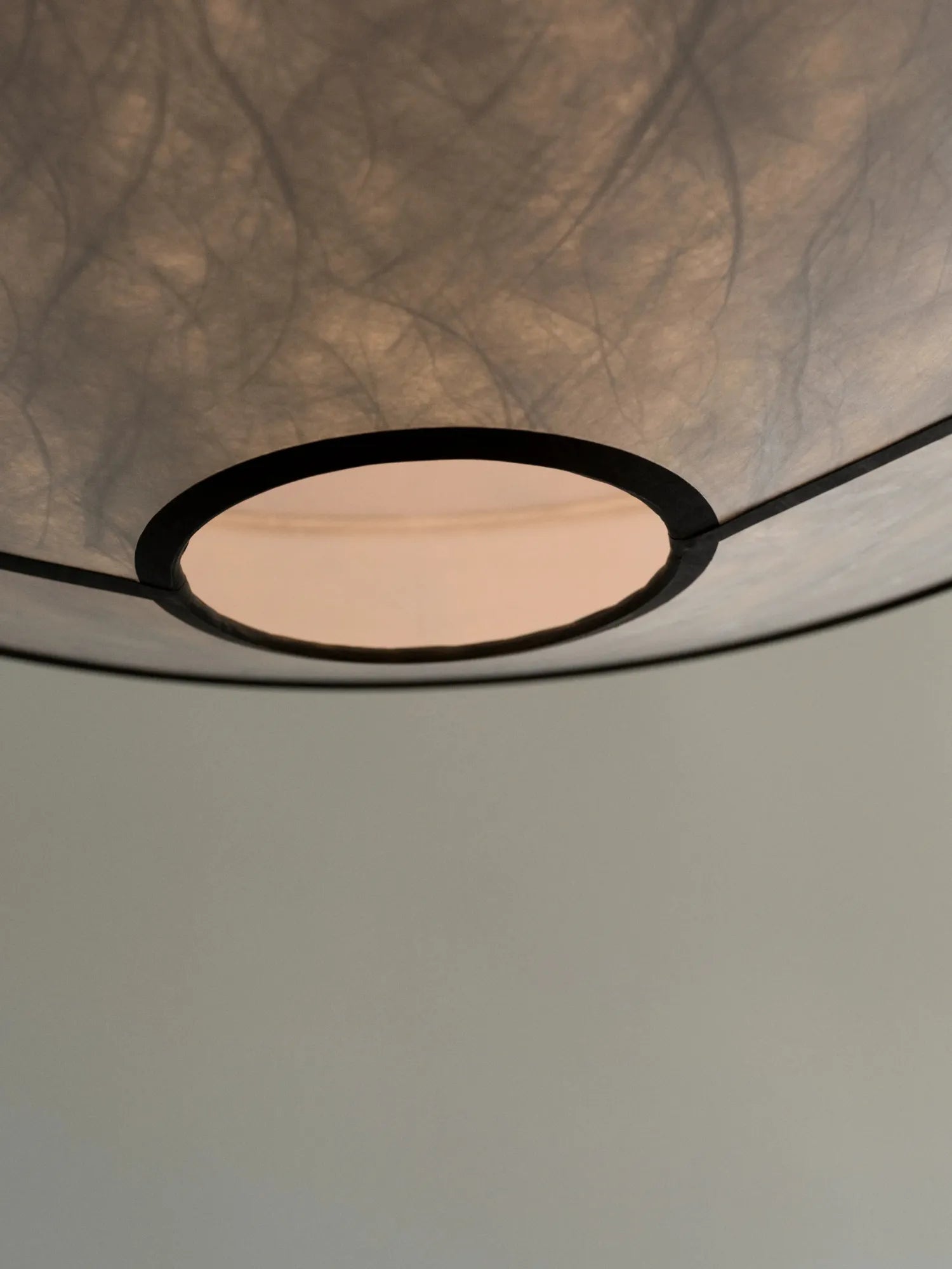 New Works Kite Pendant Lamp close-up, revealing its unique textured translucent white paper shade with dark linear patterns and a black rim around a central opening radiating warm, ambient light. Perfect for modern, stylish interiors.