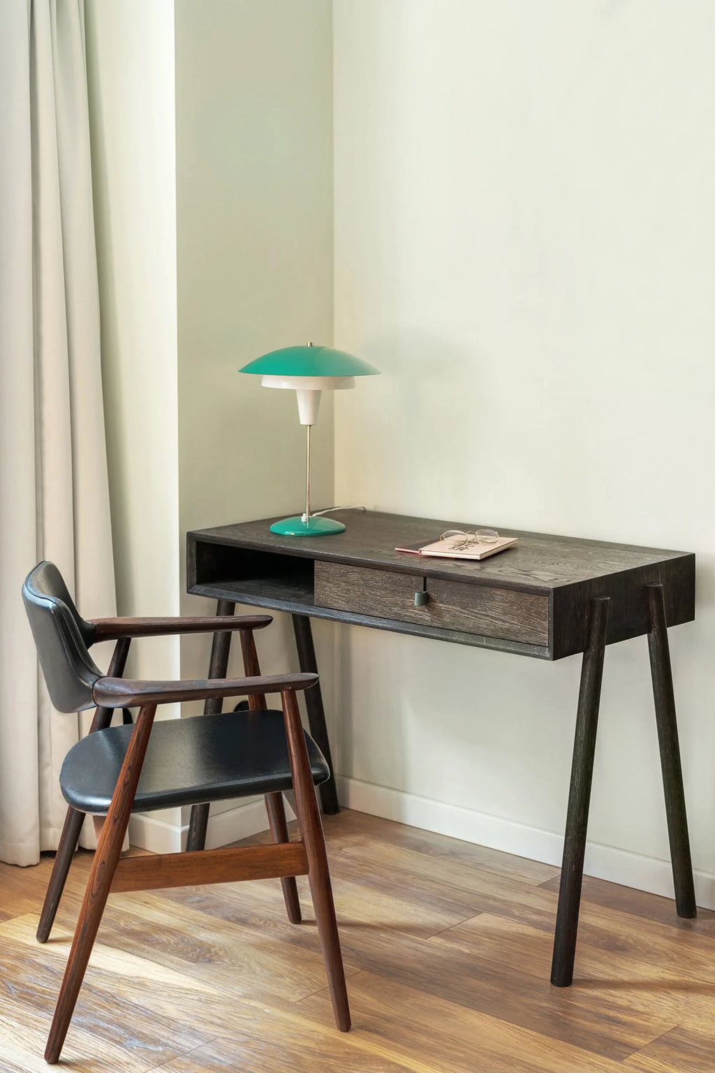 TAMO Amelia Desk: a dark brown hardwood desk with one drawer and slender tapered legs, styled with a modern teal lamp and a notebook. This luxury desk is ideal for a home office.