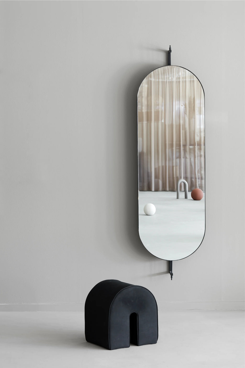Kristina Dam Full Size Rotating Mirror, a sleek modern minimalist full-length mirror featuring an elongated capsule shape and a matte black metal frame. This contemporary design includes a functional rotating mechanism, allowing the mirror to pivot on its wall-mounted matte black metal rod. Ideal as a stylish entryway mirror, bedroom accent, or for adding organic modern elegance to Scandinavian-inspired interiors.