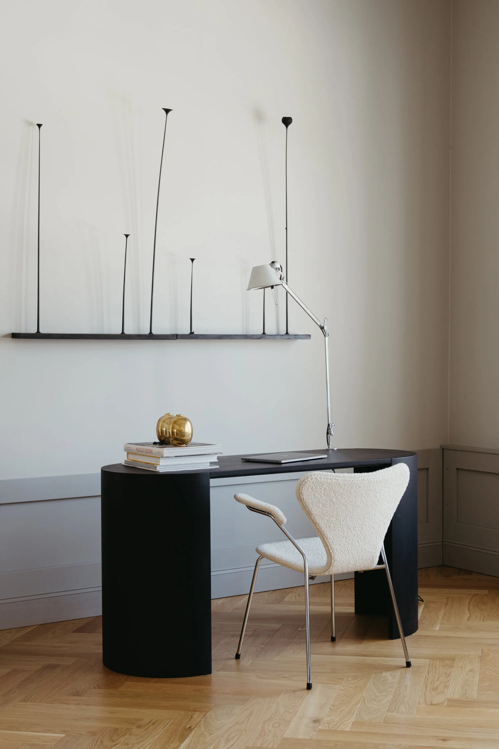 Made by Choice Airisto Desk in a stylish office setting, featuring a black wooden desk with curved legs, paired with a white bouclé chair, a silver desk lamp, and decorative items, on a wooden floor.