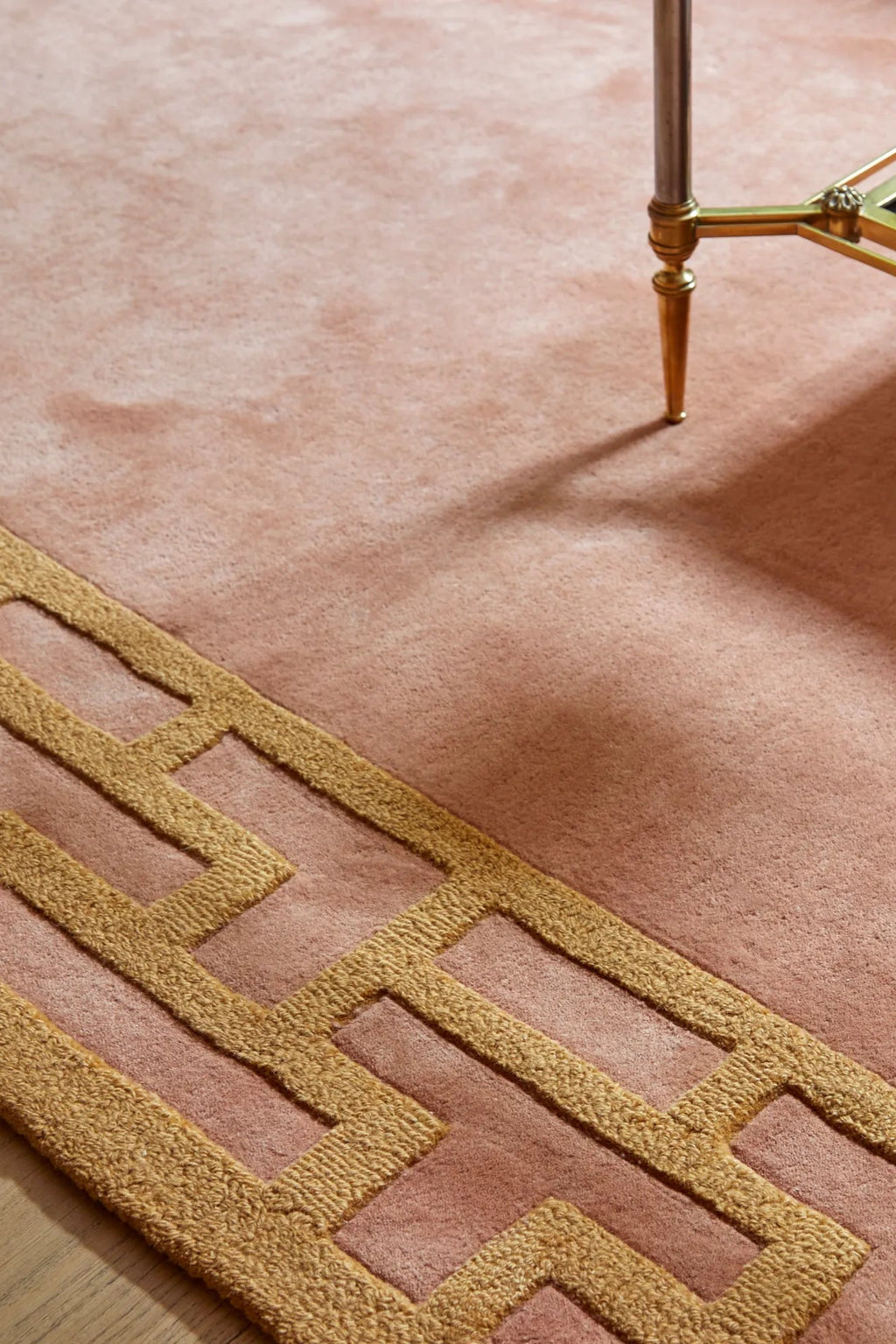 Layered Indocine Wool Rug, a luxurious blush pink wool rug with a textured gold geometric border pattern. Perfect as a stylish area rug for modern living rooms or bedrooms.
