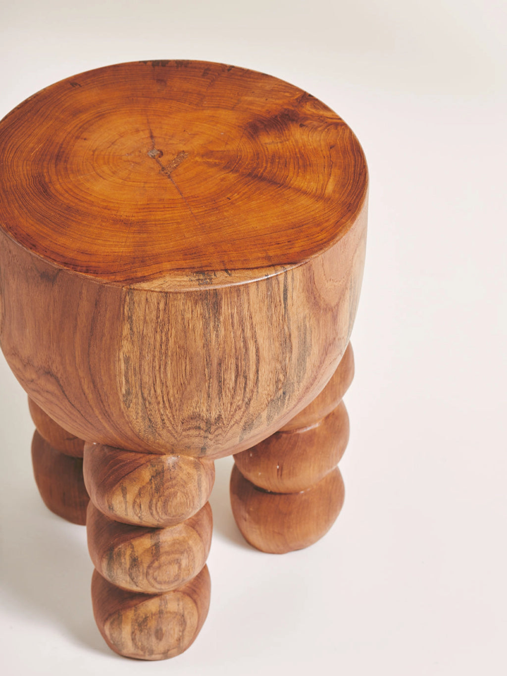 Heaps & Woods Alice Stool, a solid wood round stool crafted from rich, warm brown wood with visible tree rings on its top surface and a smooth, sculptural bulbous body. It features three chunky, stacked-sphere-like legs, giving it an organic modern and brutalist aesthetic. Perfect as a unique accent stool or side table for natural living room decor or a rustic bedroom.