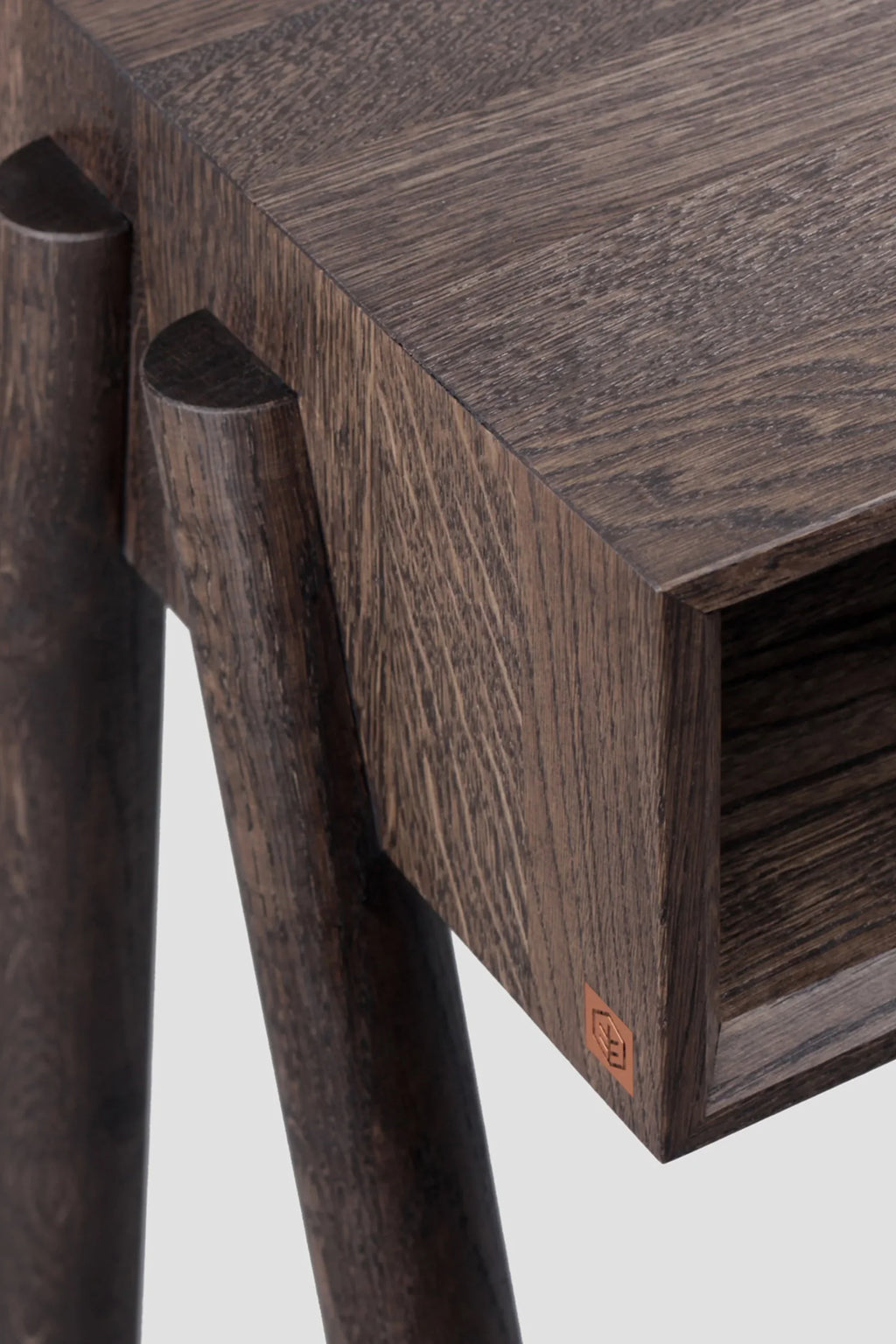 TAMO Amelia Desk close-up, showing rich dark brown wood grain, a cubby shelf, and an embossed copper logo. This premium handcrafted desk is perfect for a modern office.