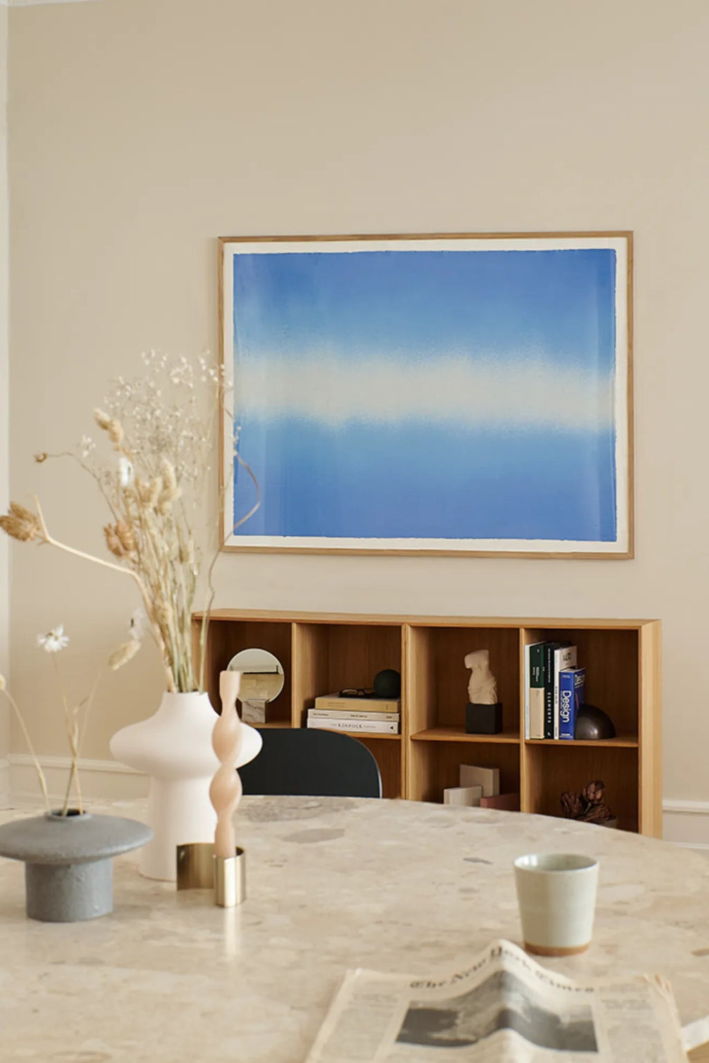 The Poster Club Blue Interstellar, an abstract art print featuring a serene horizontal gradient of deep royal blue fading into soft sky blue and white, creating a tranquil cloud-like effect. This minimalist poster is presented in a light natural oak frame, enhancing its contemporary aesthetic. Perfect as modern wall art for Scandinavian living rooms, serene bedrooms, or a refined dining room gallery wall.