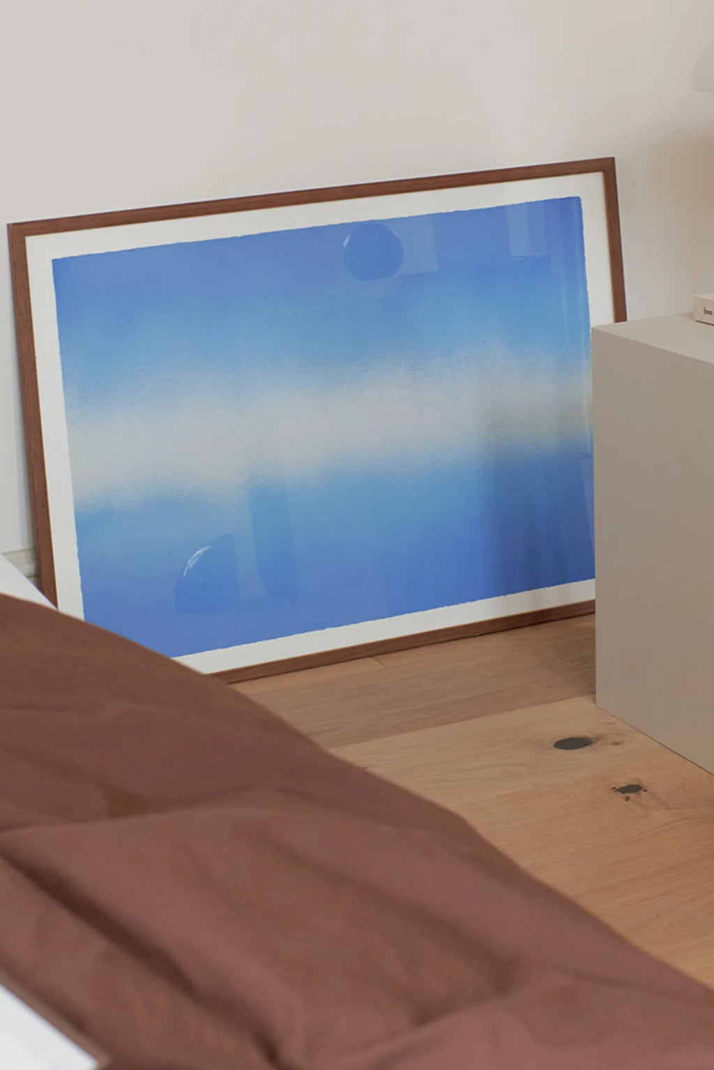 The Poster Club Blue Interstellar, a modern abstract art print featuring a serene gradient design that transitions from deep sky blue to soft white, accented by subtle atmospheric circular elements, framed in a warm natural wood frame with a crisp white mat. This contemporary framed wall art is perfect for minimalist living rooms, tranquil bedrooms, or adding a calming focal point to any gallery wall.