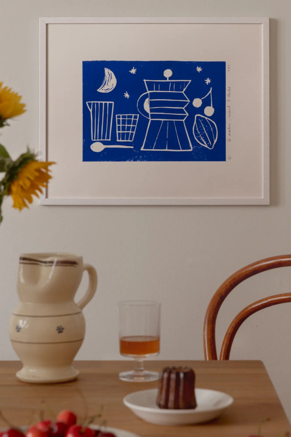 The Poster Club Aube, a vibrant royal blue art print featuring a minimalist white linocut-style illustration of breakfast elements including a moka pot, moon, stars, cherries, and a.