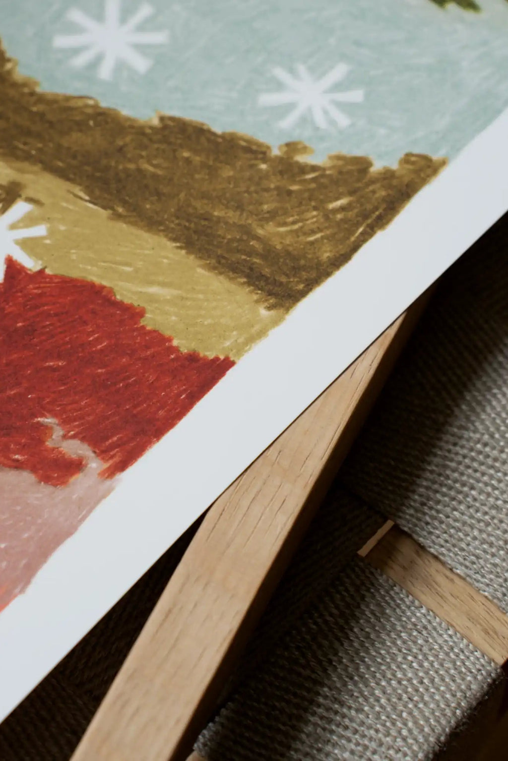 The Poster Club The House and the Hills, an abstract landscape art print featuring bold blocks of red, olive green, and brown, topped by a light blue sky with graphic white snowflake shapes, all rendered.