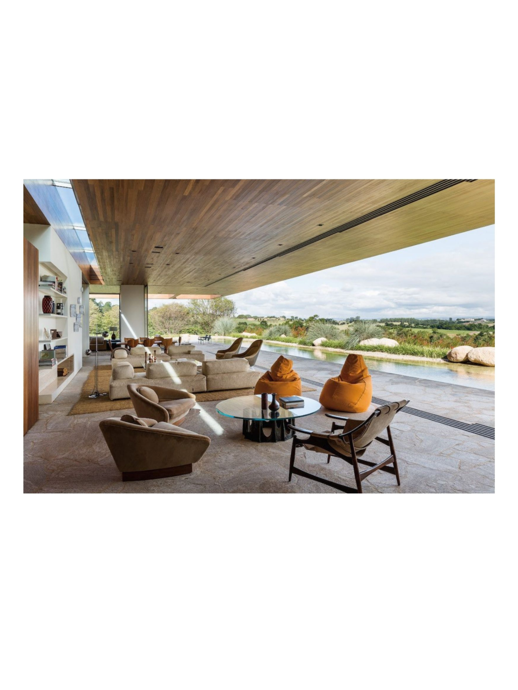 Book Arthur Casas: Architecture, showcasing a luxurious open-plan living room with wood-paneled ceilings, light-colored modern furniture, and floor-to-ceiling windows overlooking a natural landscape and water feature. This premium architecture book is perfect for design enthusiasts and professionals seeking inspiration in contemporary home design.