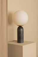 Table lamp with a spherical white shade and dark base on a beige pedestal against a beige wall.